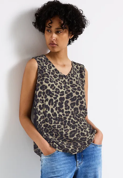 Frau mit lockigen Haaren trägt ärmelloses Leoparden-Top und Jeans.